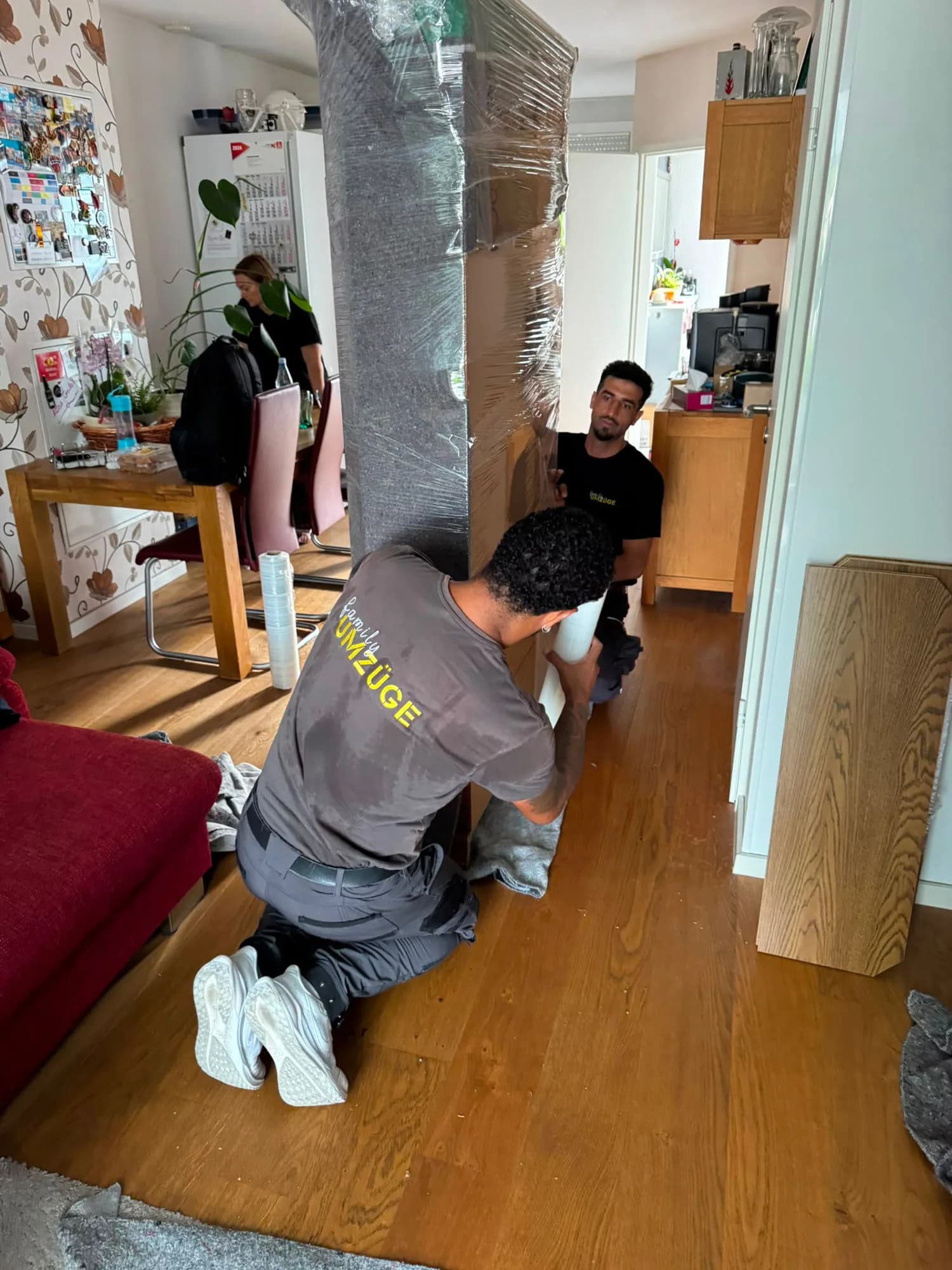 Team von Family Umzüge umwickelt ein großes Möbelstück sorgfältig mit Schutzfolie im Wohnzimmer